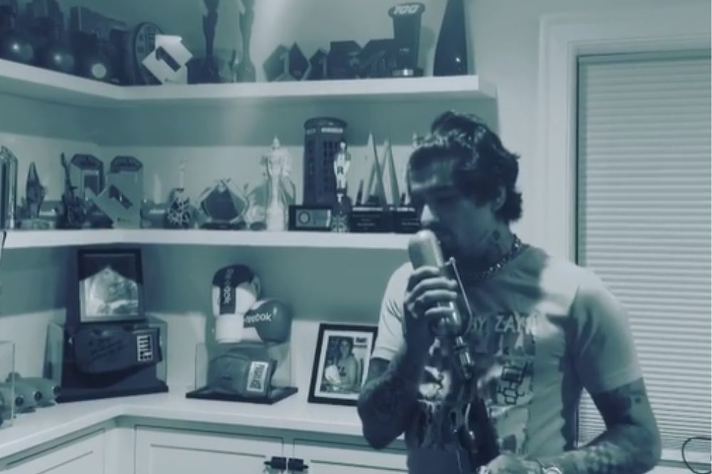 Imagem em preto e branco de Zayn segurando um microfone em um quarto com uma estante ao fundo