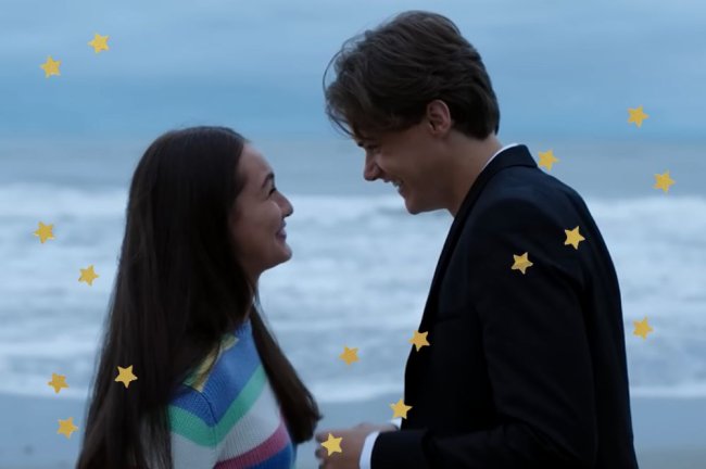 Blooper of The Summer That Changed My Life with actors Lola Tung and Christopher Briney as Belly and Conrad laughing while looking at each other on a beach with the sea in the background