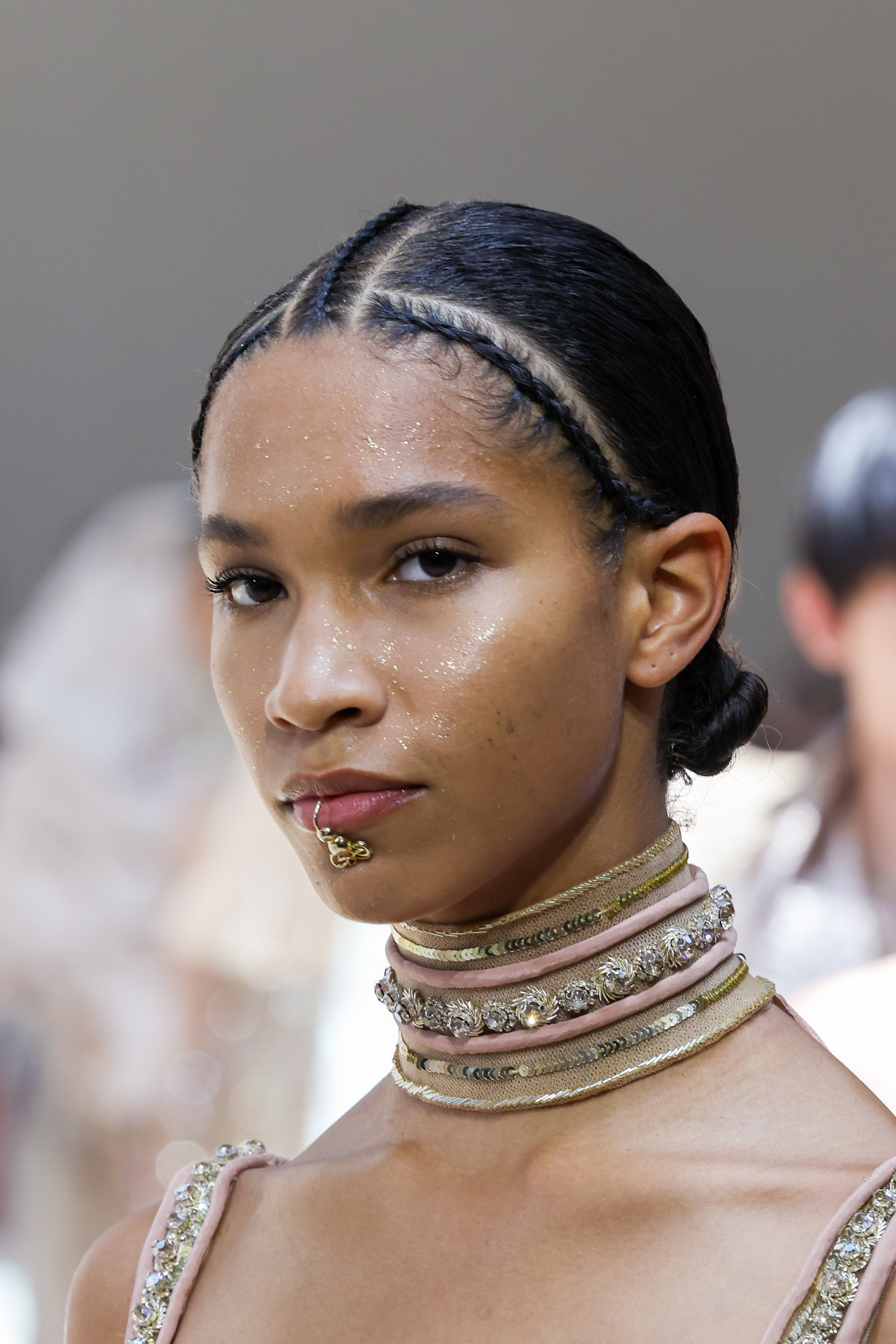 Modelo com penteado com trança de raiz e space buns baixo e glitter no rosto no Desfile de outono-inverno 2022-23 da Elie Saab na semana de alta-costura em Paris