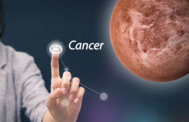 Uma mão toca em cima do símbolo do signo de câncer; o planeta vênus está posicionado à direita na imagem