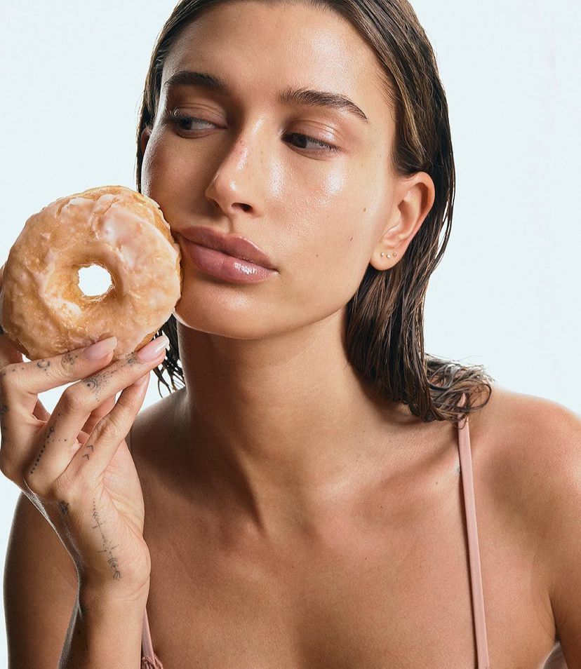 Imagem mostra Hailey Bieber posando um donuts em campanha promocional para a Rhode, sua marca de produtos de skincare.