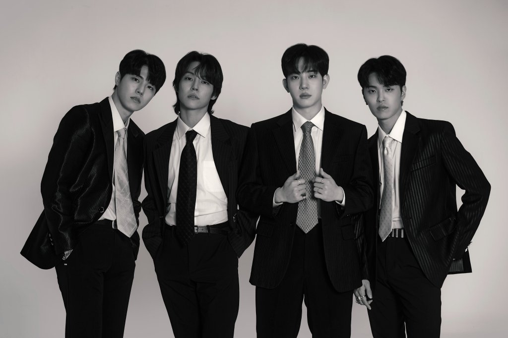 Quatro integrantes do grupo The Rose em uma foto preto e branco usando ternos e gravata com expressões sérias e neutras
