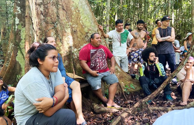 Fotos de um grupo de pessoas conversando no pé de uma árvore, no meio da Floresta Amazônica