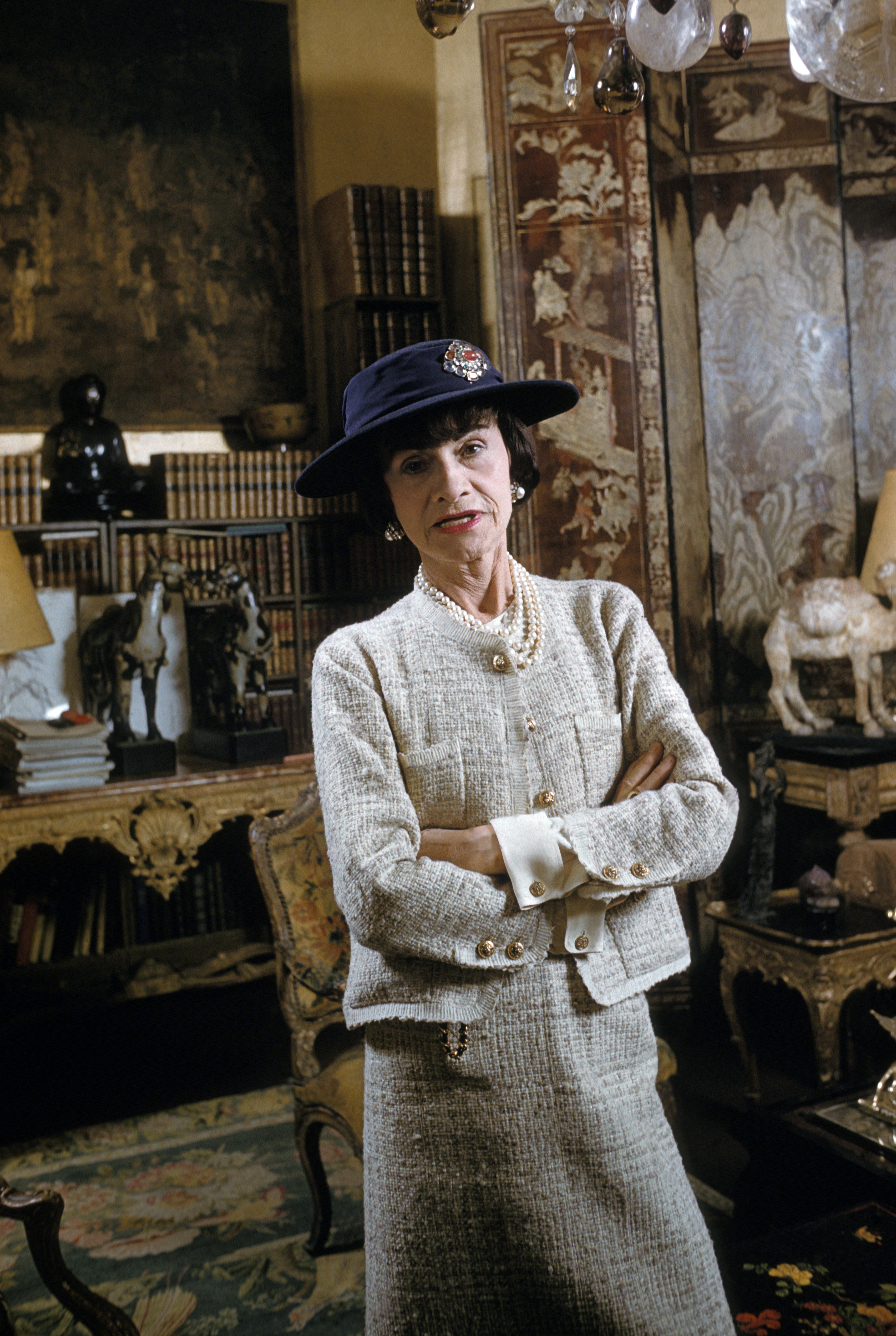 Coco Chanel em seu apartamento na rue Cambon, em Paris, em 1954, usando chapéu e tailleur de tweed com botões dourados