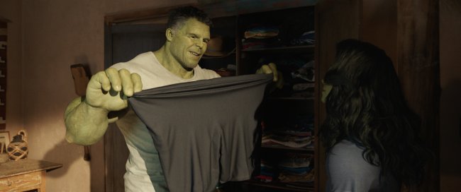 Hulk e Mulher-Hulk conversando. Ele segura uma camiseta preta esticada.