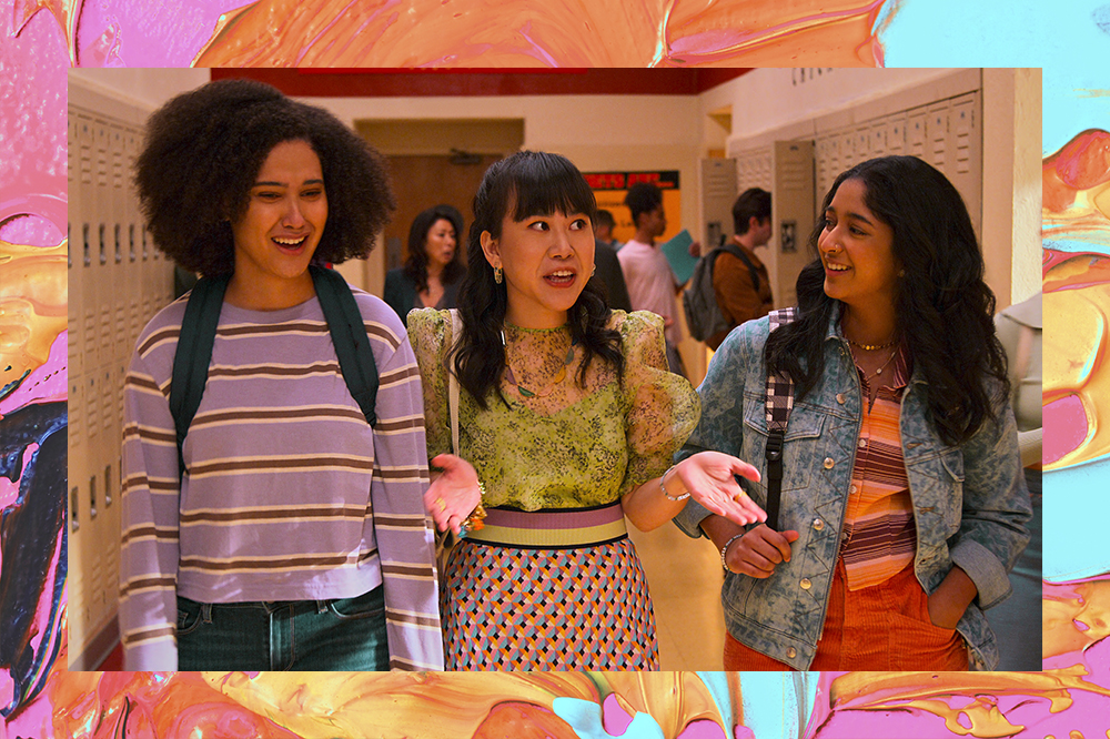 Cena da série Eu Nunca... em que Fabiola, Eleanor e Devi estão conversando no corredor da escola. A montagem tem fundo laranja, rosa e amarelo