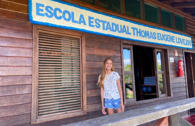 Estudante ribeirinha do Amazonas posa na fachada da escola em que estuda, de madeira. A menina é lora é tem 15 anos.