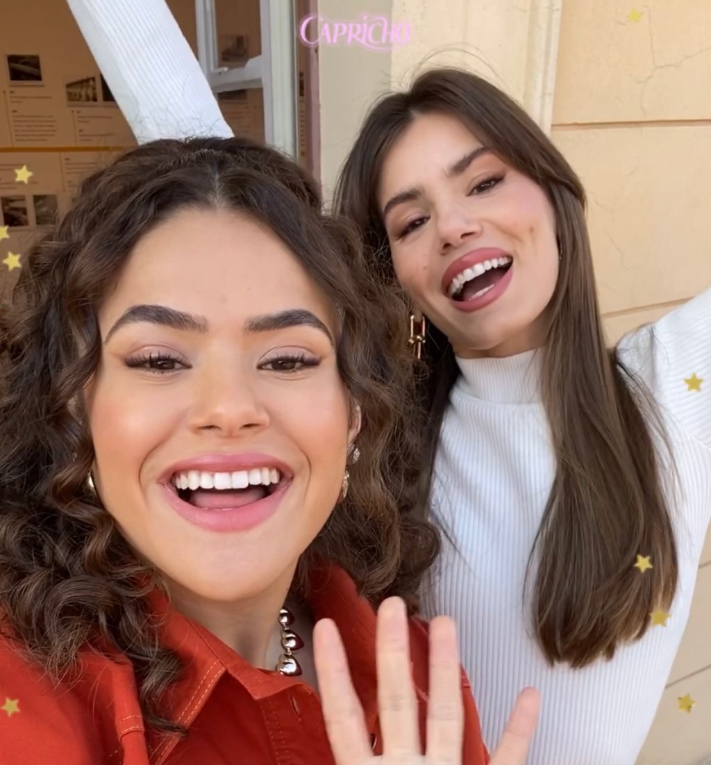 Maisa e Camila Queiroz sorrindo para a câmera; o logo da Capricho aparece em rosa na parte superior da foto; estrelas amarelas decoram a imagem