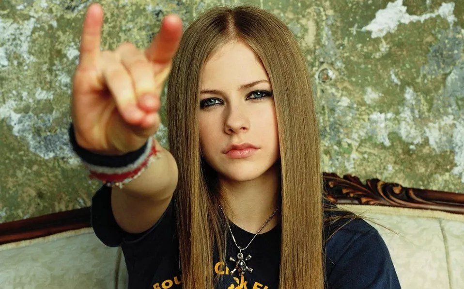 Foto antiga da Avriel Lavigne fazendo sinal de rock and roll com a mão