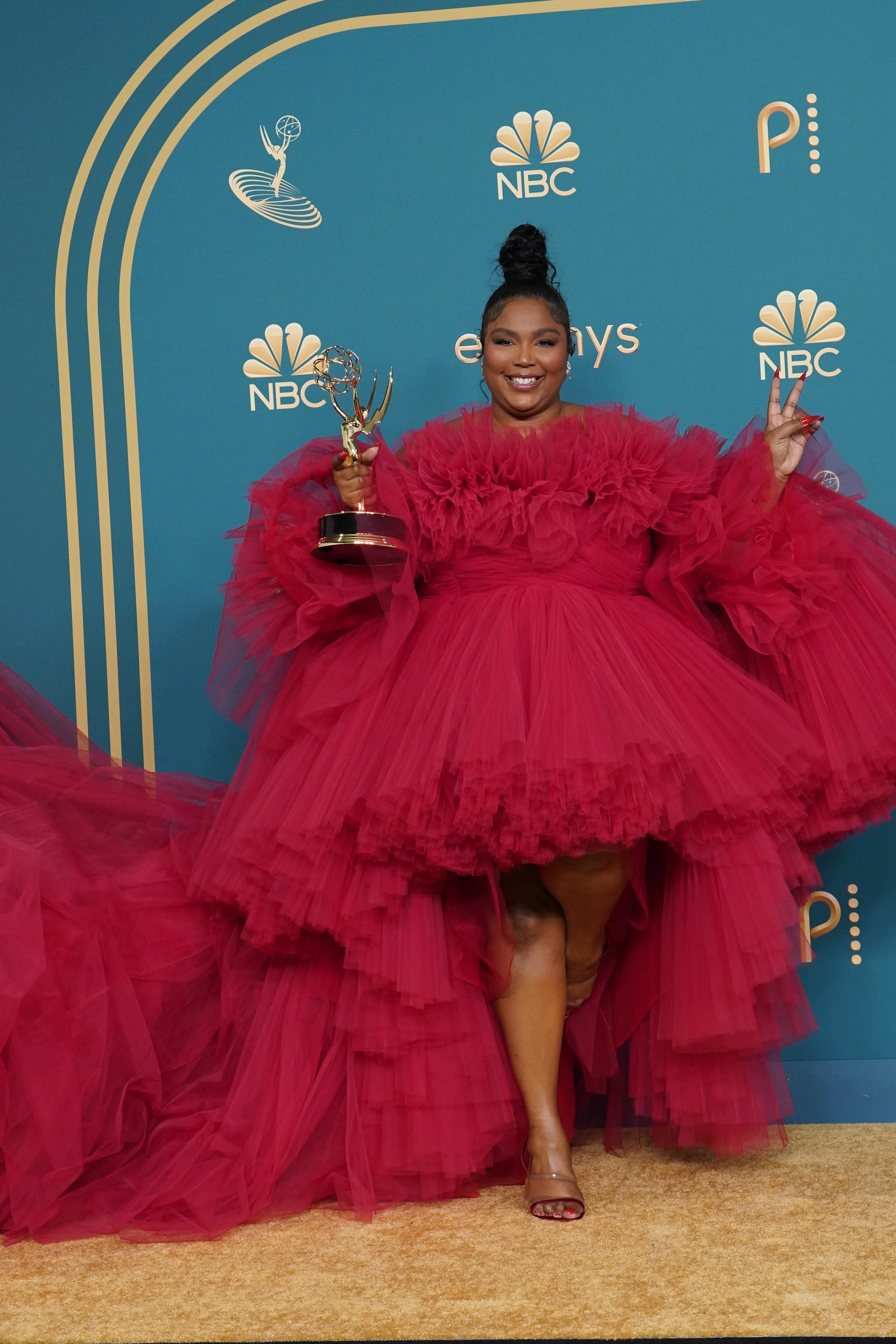 Lizzo no Emmy Awards 2022 sorrindo, segurando prêmio e usando vestido vermelho de tule curto na frente e longo atrás