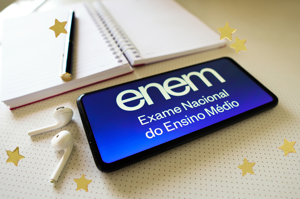 Foto de um celular aberto na página do Enem, posicionado em frente a um aderno e uma caneta