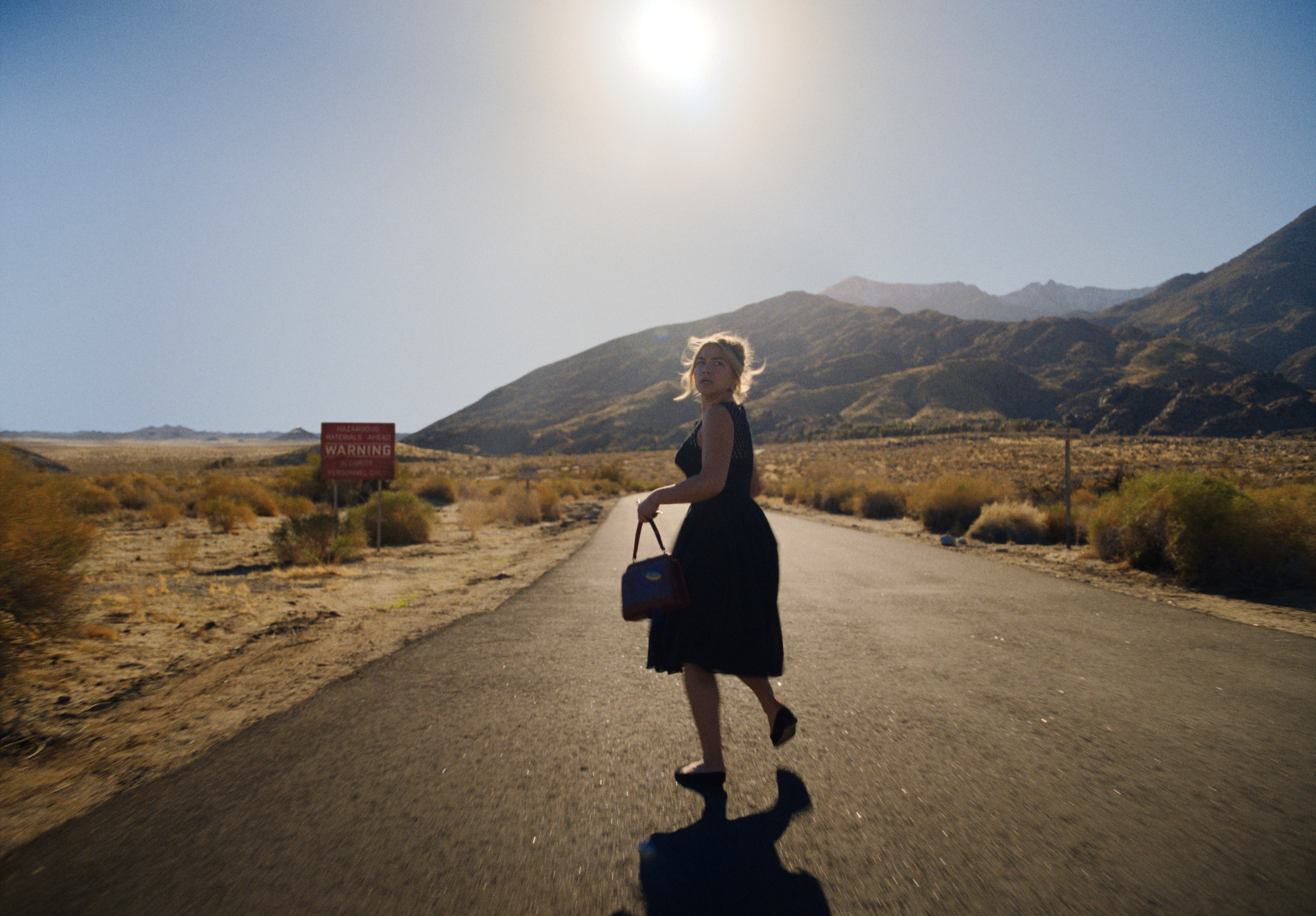 Florence Pugh como Alice correndo em estrada usando vestido preto em cena do filme Não Se Preocupe, Querida