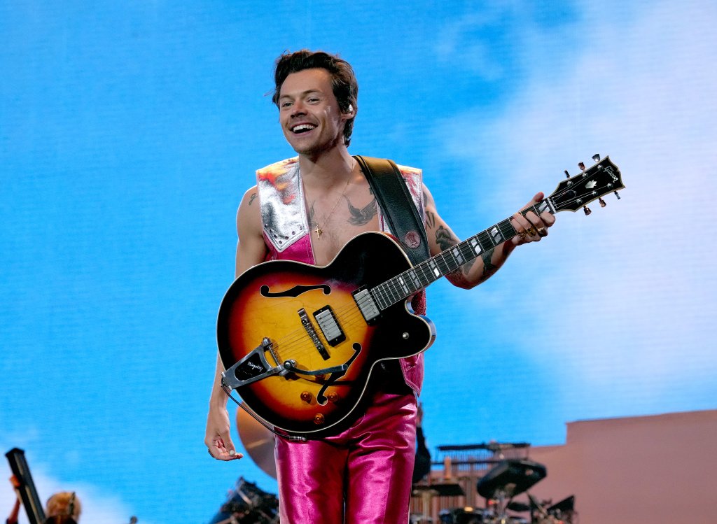 Harry Styles se apresentando no Coachella 2022 sorrindo enquanto segura violão