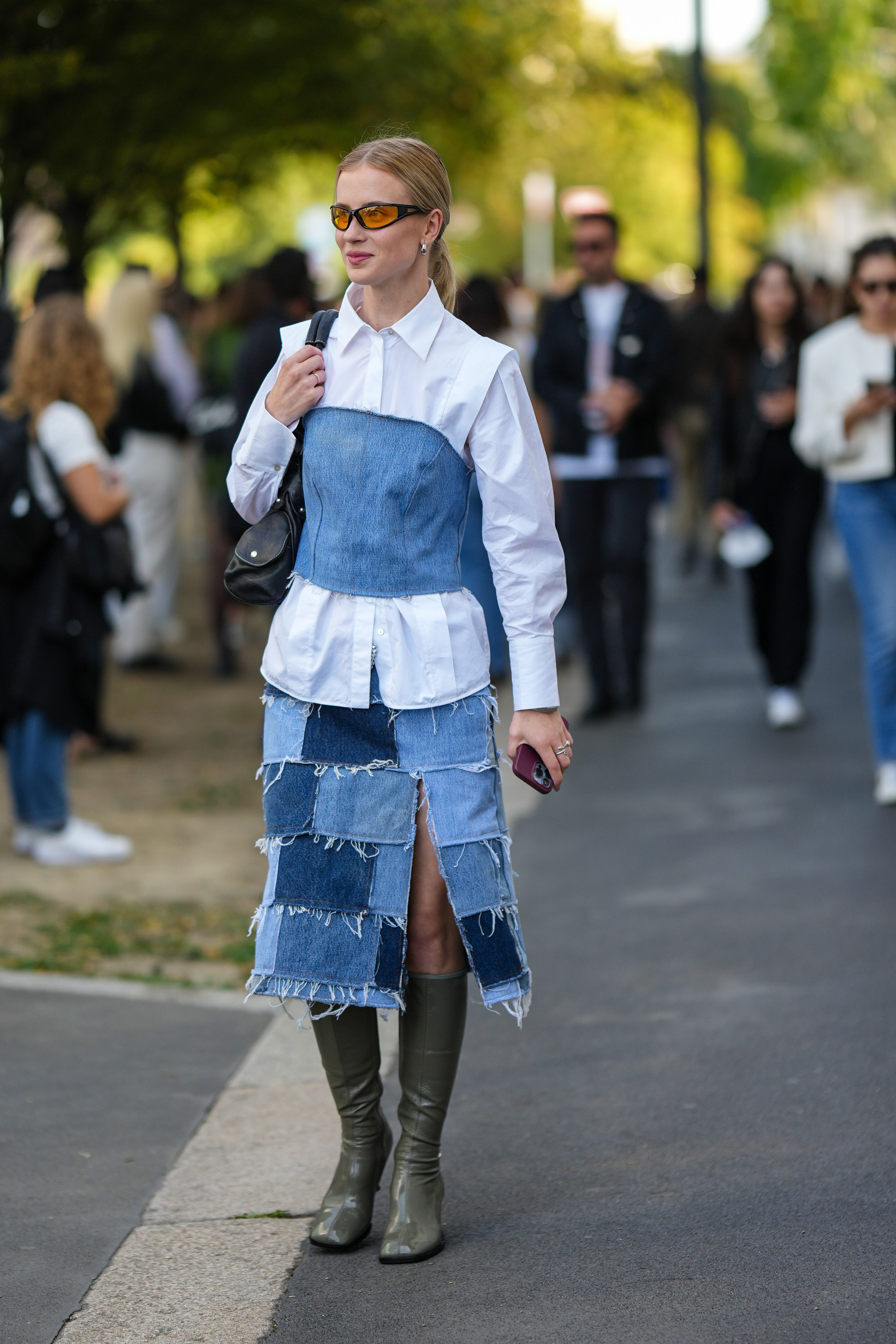 Mulher usando camisa branca com top jeans por cima, saia jeans e bota verde no street style da semana de moda de Milão