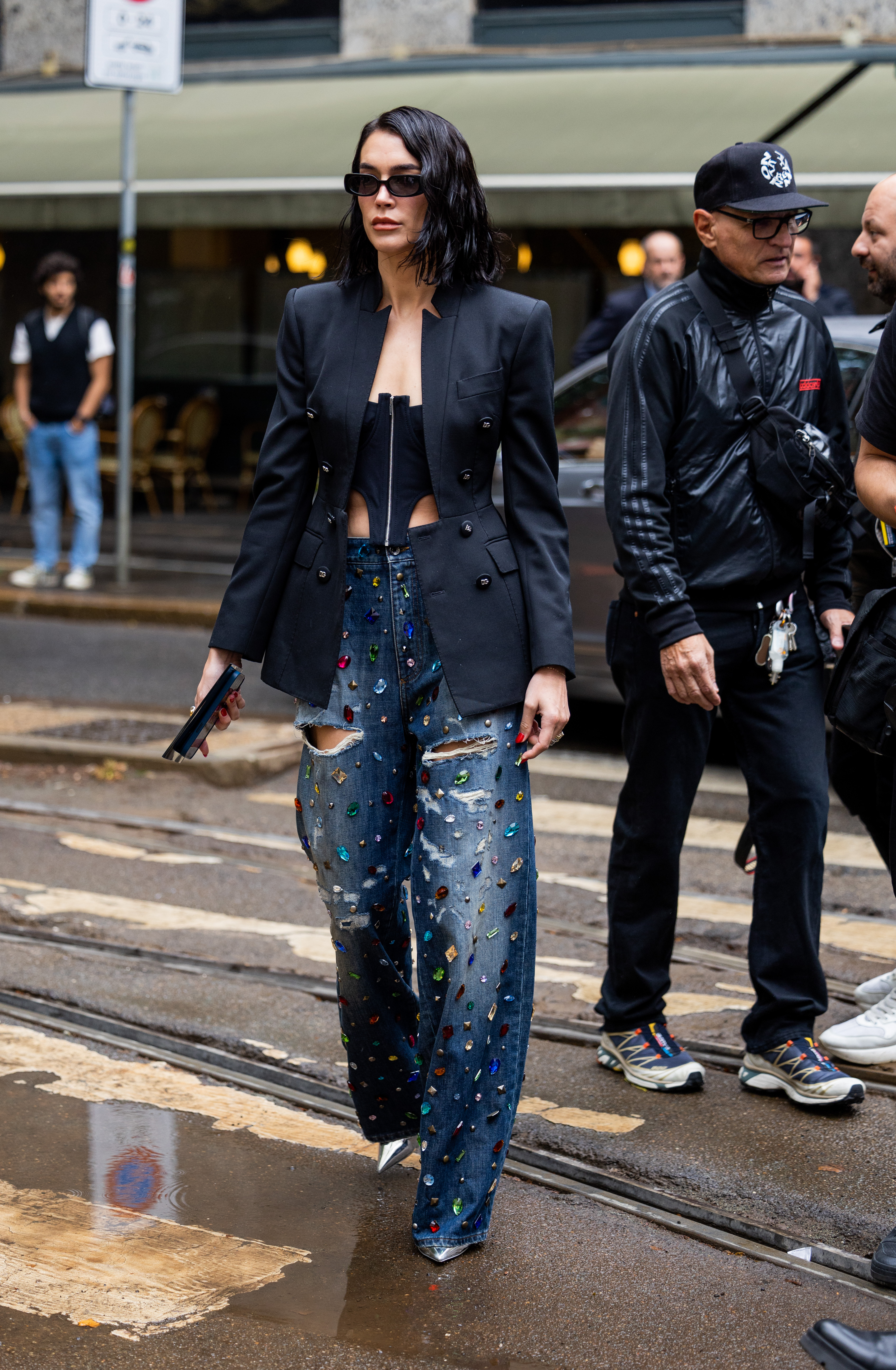 Mulher usando blazer e corset preto com calça jeans com aplicações de pedras coloridas no street style da semana de moda de Milão