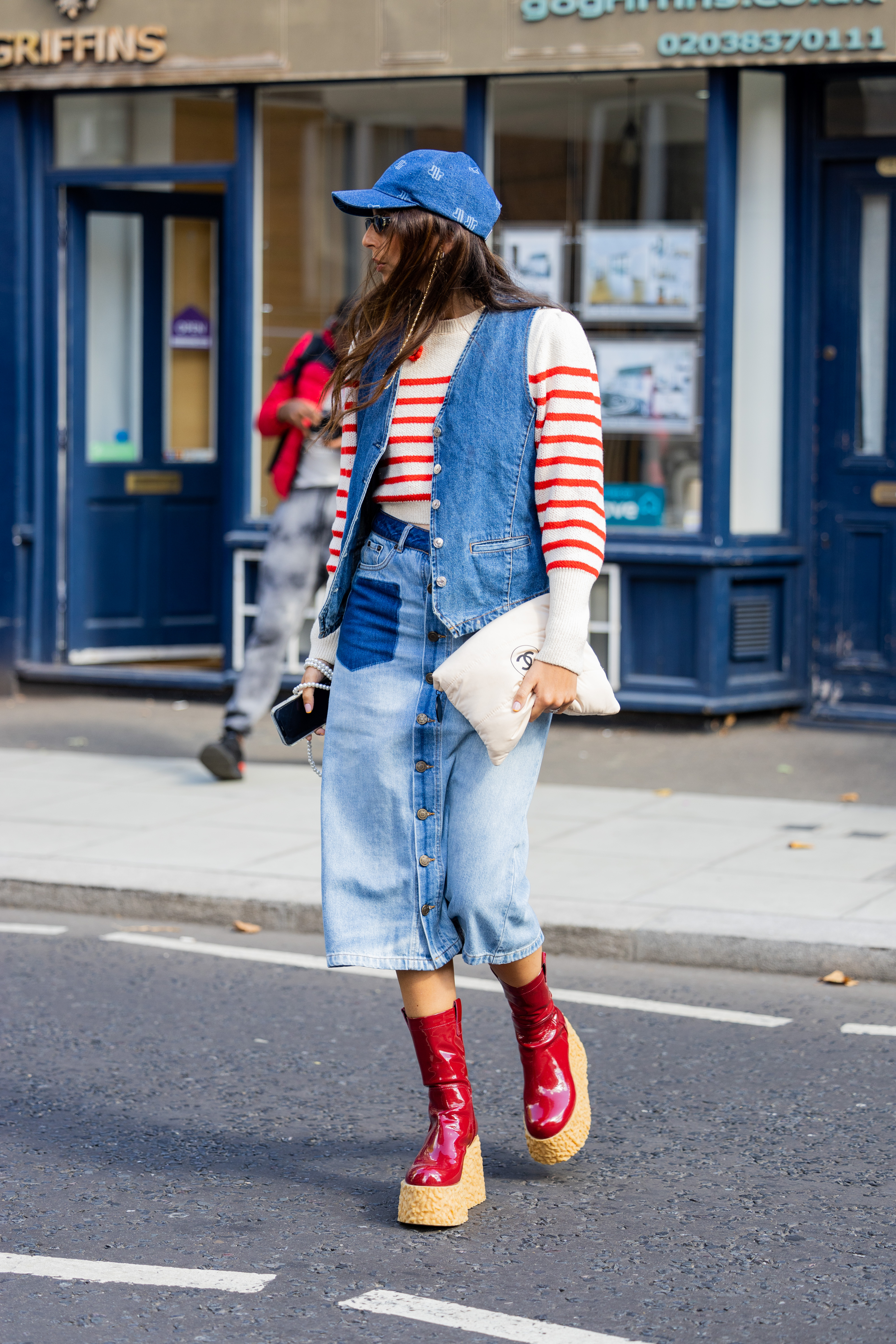 Gabriella Berdugo usando tricô vermelho e branco, colete jeans, saia longa jeans e bota vermelha vinil na semana de moda de Londres