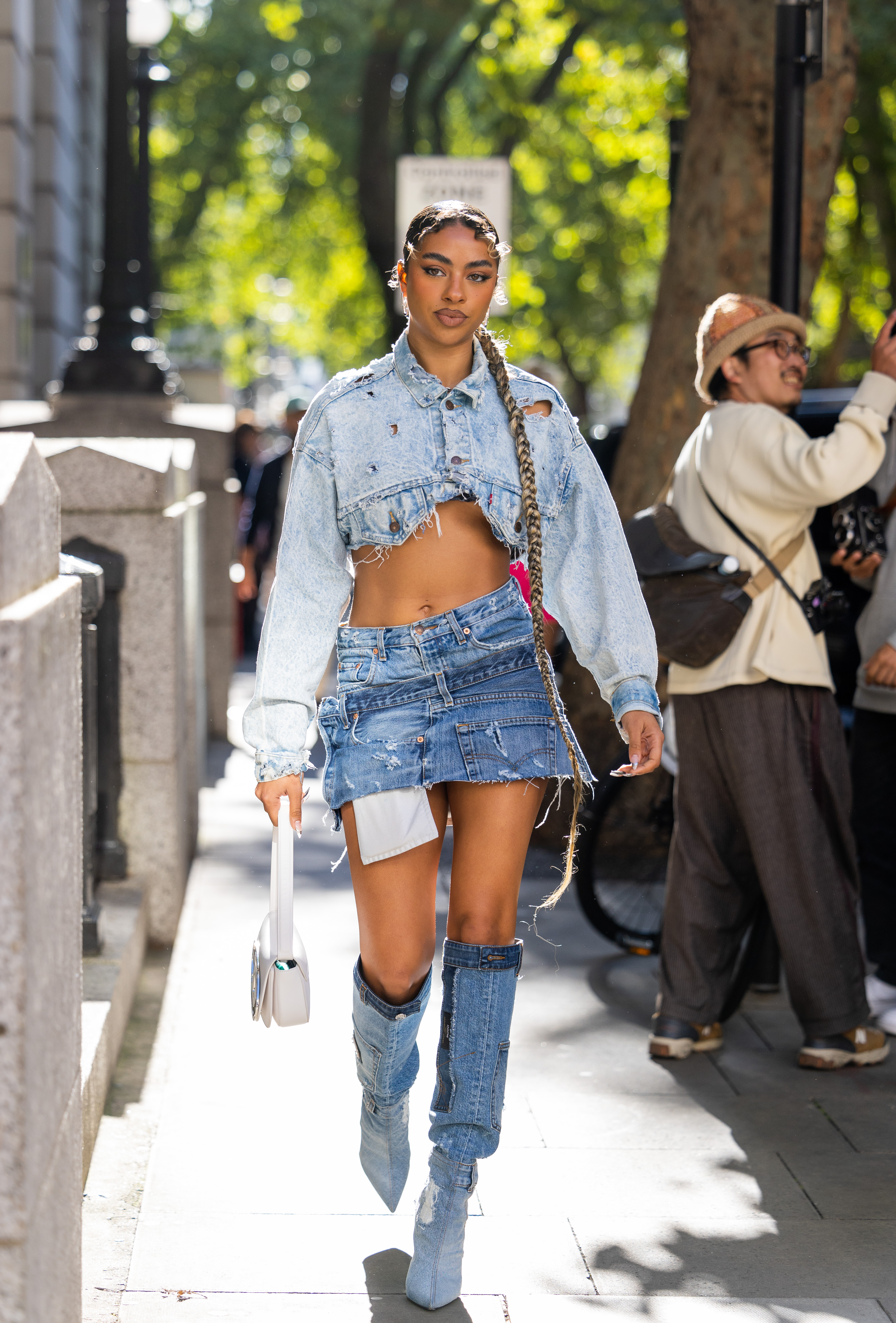 Garota usando look com jaqueta jeans cropped, minissaia jeans e bota jeans na semana de moda de Londres