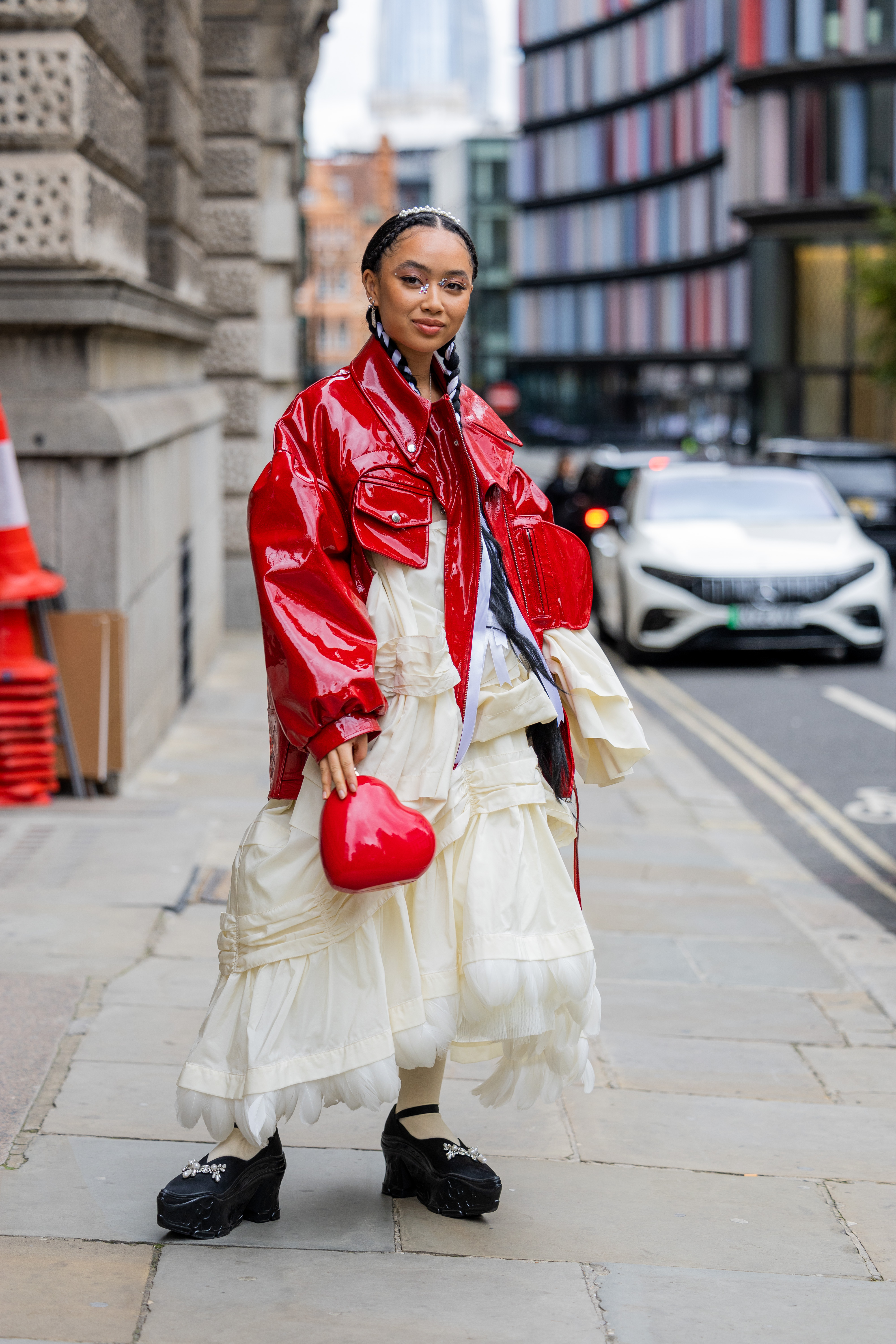 Griff usando jaqueta vermelha de vinil, vestido off white de babados, bolsa de coração e sapato preto no street style da semana de moda de Londres