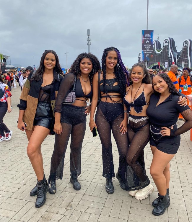 Foto de cinco meninas com look all black no Rock in Rio 2022. Todas elas olham para a câmera e sorriem para a foto.