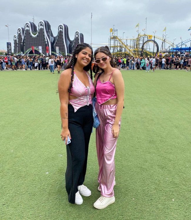 Foto de duas meninas no Rock in Rio 2022. Ambas usam looks com peças rosas, olham para a câmera e sorriem.