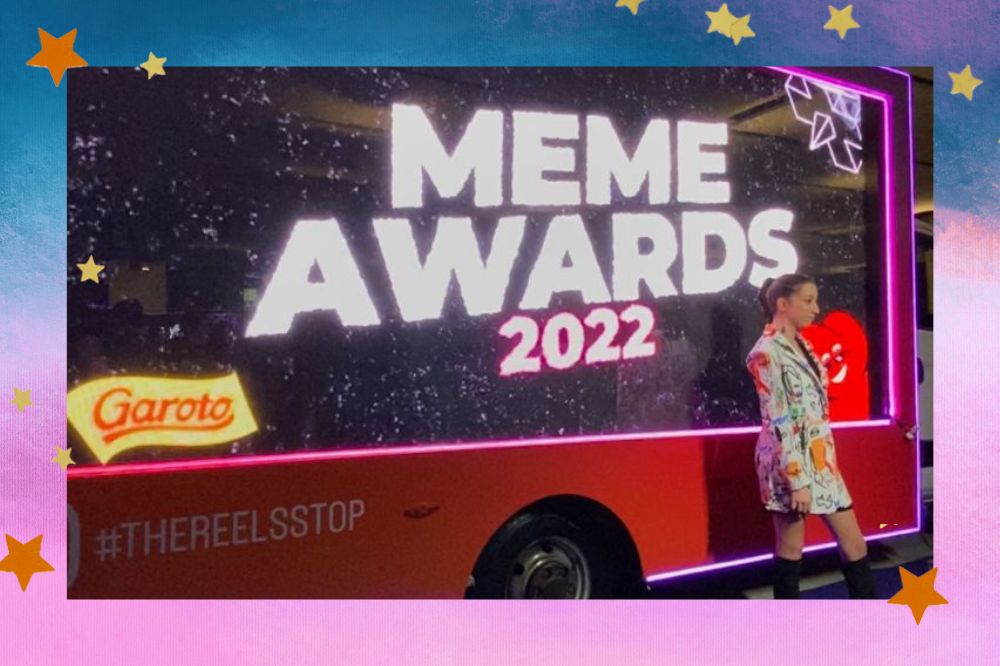 Painel do Meme Awards ao fundo e mulher posando para foto