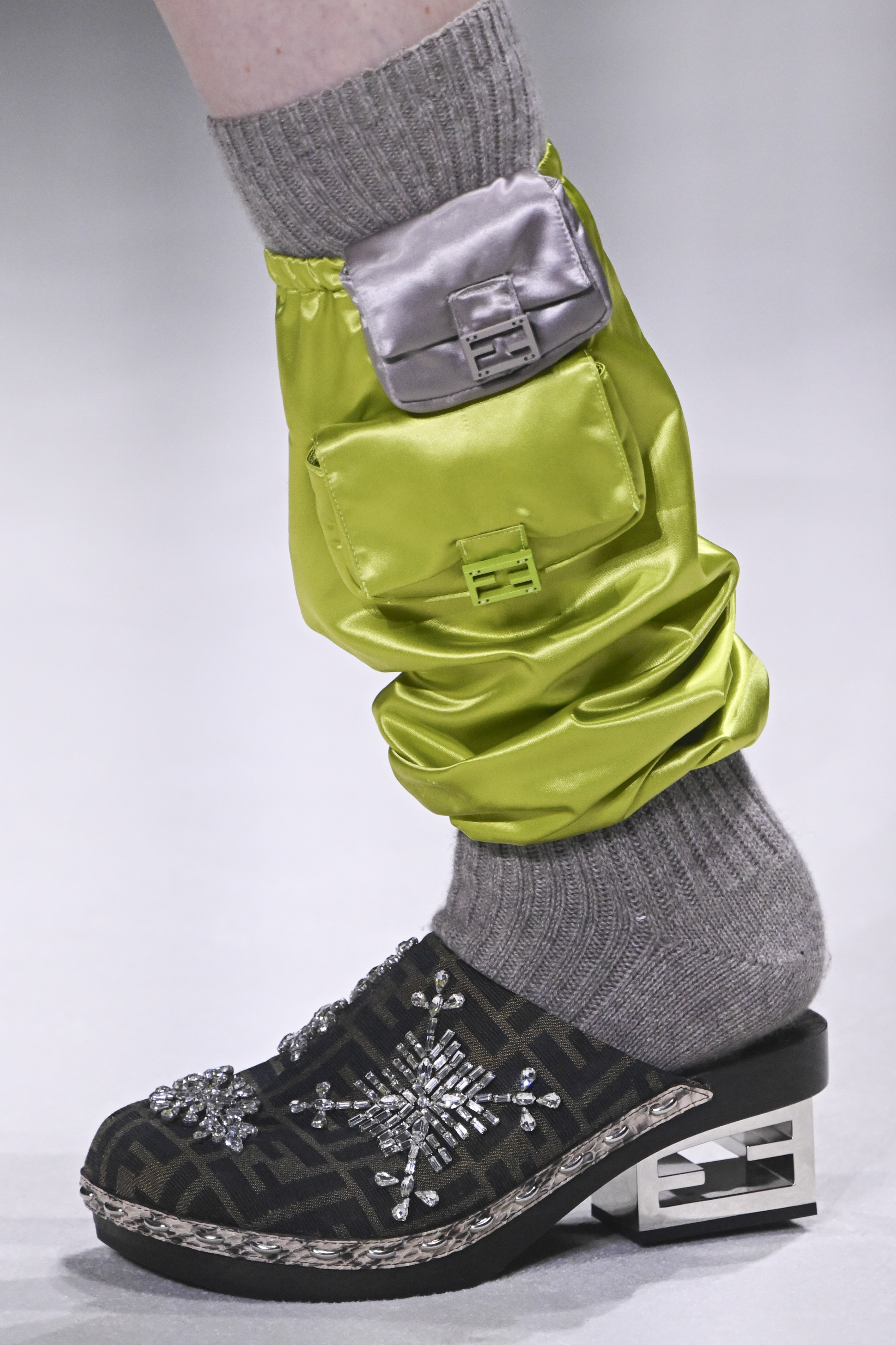 Desfile de primavera-verão 2023 da Fendi na semana de moda de Nova York. Pé de modelo usando sapato clog com meia cinza e polaina verde neon com duas minibolsas acopladas