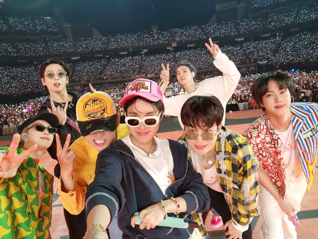 BTS posando pra selfie com plateia em show ao fundo