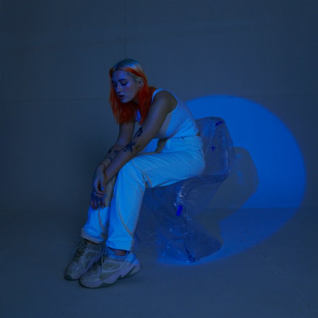 Gab Ferreira posando em um fundo azul usando roupa branca com iluminação também azul no cenário