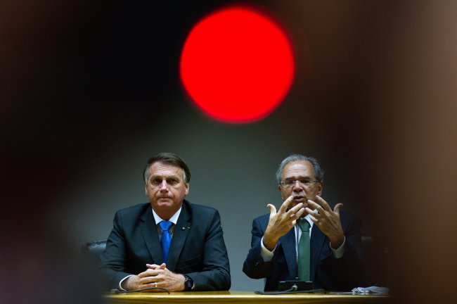 Jair Bolsonaro e Paulo Guedes gesticulam durante palestra; ambos são homens brancos, por volta dos 60 anos