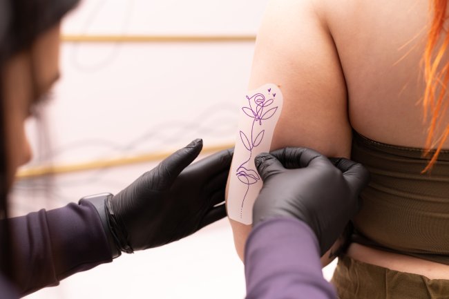 Mão de uma tatuadora medindo o decalque da tattoo no braço da cliente