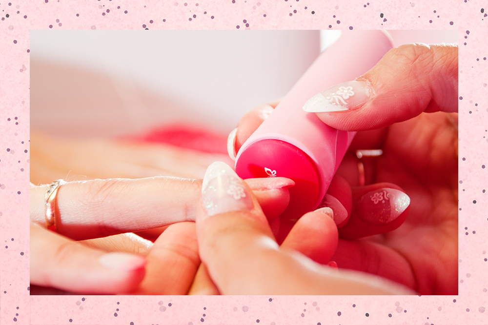 Montagem em fundo rosa com bolinhas. Na foto, há as mãos da manicure fazendo a mão de uma jovem. Ela está aplicando um carimbo de nail art em uma das unhas.