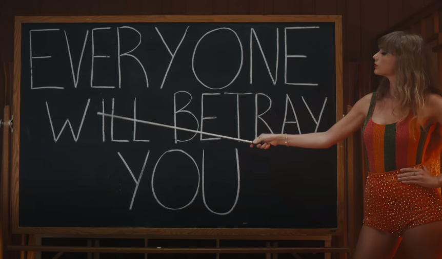 Taylor Swift no clipe de Anti-Hero ao lado de uma lousa escrito 