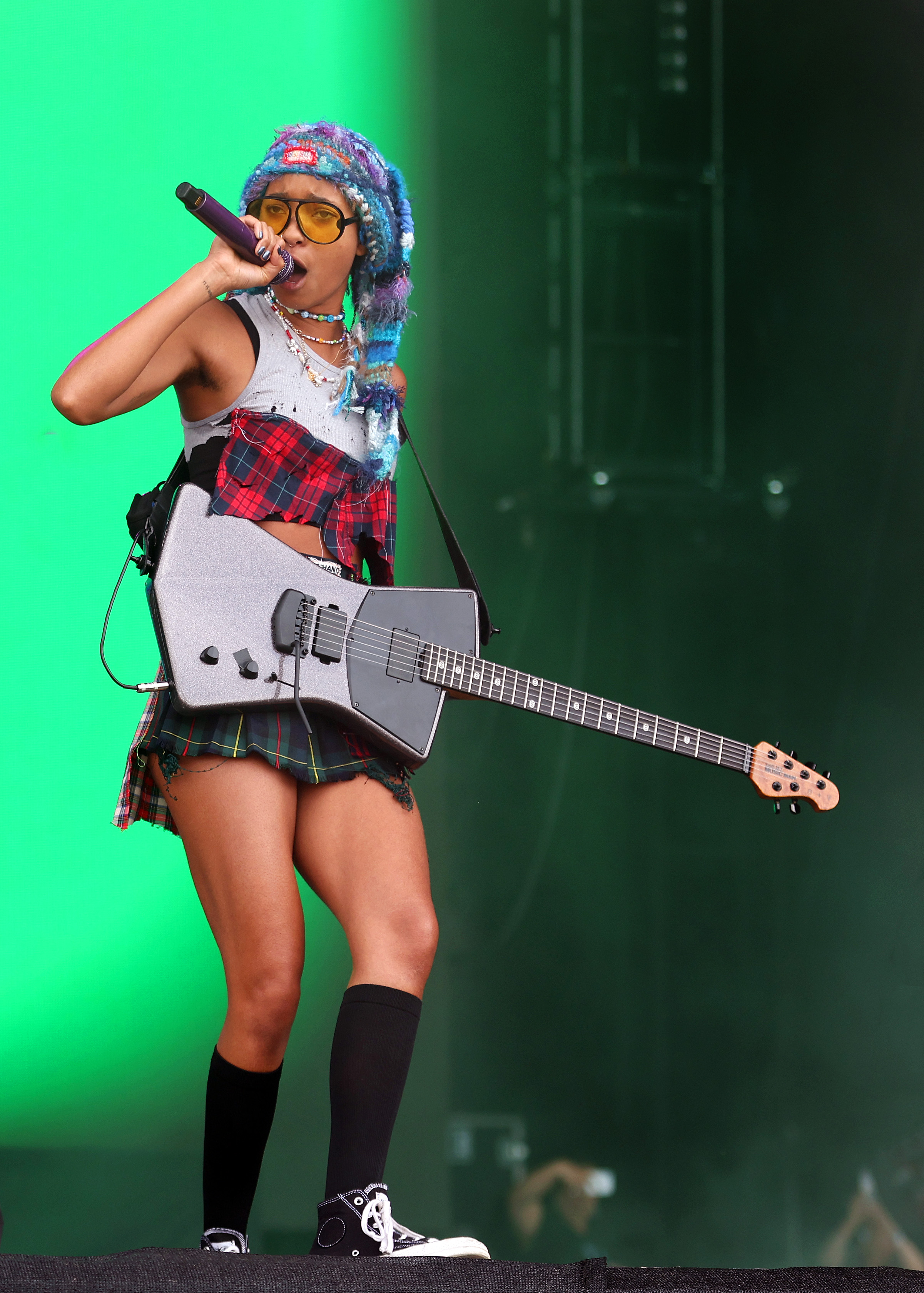 Reading Festival 2022 – Day 3 Willow Smith no Reading Festival em agosto de 2022 usando camiseta branca com estampa xadrez, minissaia e meia preta com tênis preto enquanto canta e toca guitarra