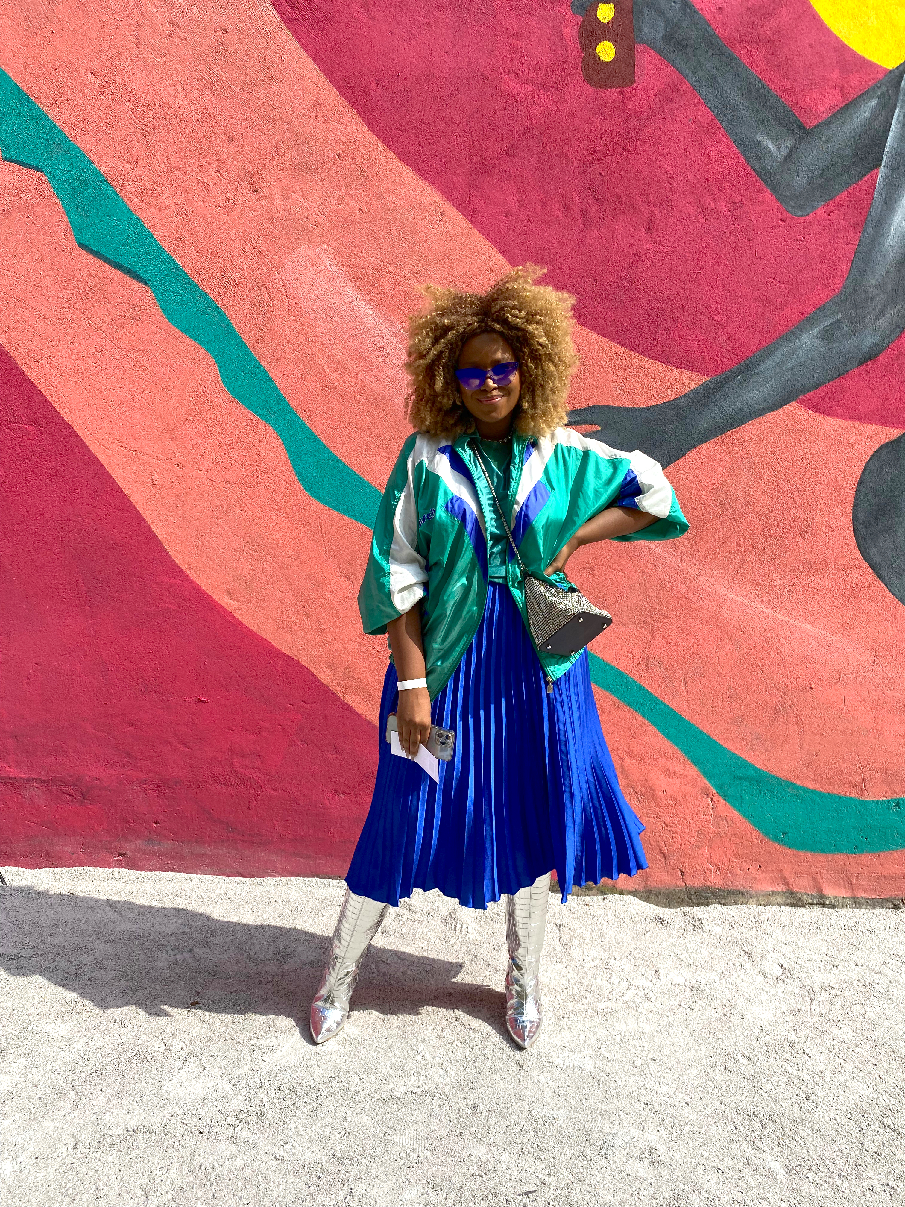 Look do São Paulo Fashion Week N54 com saia azul plissada, jaqueta bomber verde e bota prata