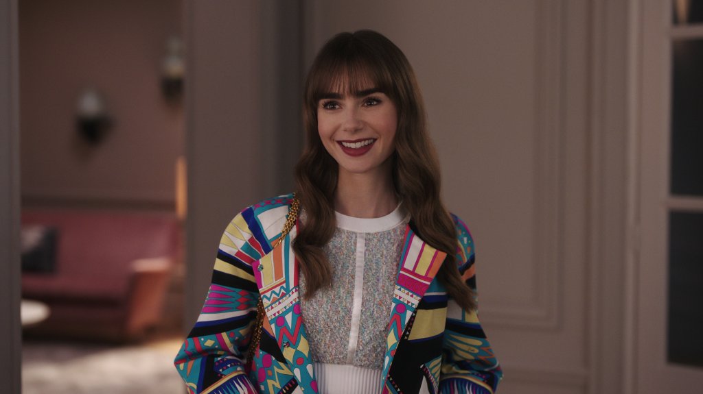 Lily Collins em cena de Emily in Paris; ela está sorrindo e olhando para frente