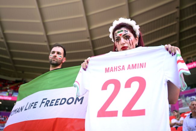 Wales v IR Iran: Group B – FIFA World Cup Qatar 2022 DOHA, QATAR - NOVEMBER 25: Fans hold up a shirt with the name of Mahsa Amini and a flag advocating for women's rights prior to the FIFA World Cup Qatar 2022 Group B match between Wales and IR Iran at Ahmad Bin Ali Stadium on November 25, 2022 in Doha, Qatar. People have continued demonstrating in Iran over the death of Mahsa Amini in September. Mahsa Amini fell into a coma and died after being arrested in Tehran by morality police, for allegedly violating the country's hijab rules. (Photo by Matthias Hangst/Getty Images)