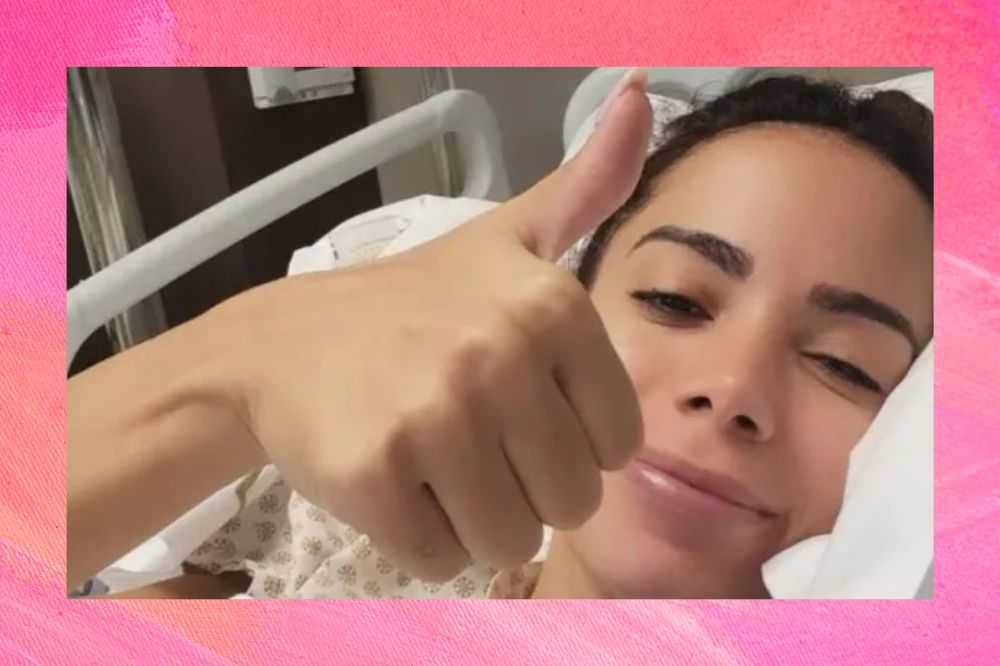 Anitta fazendo joinha com a mão em cama de hospital