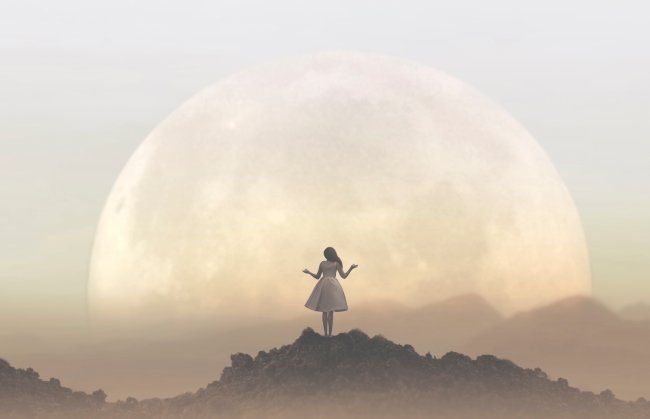Aprenda um rito de cocriação para fazer durante a última Superlua de 2022 Foto de uma mulher de vestido branco de costas, fazendo uma oração para uma lua gigante