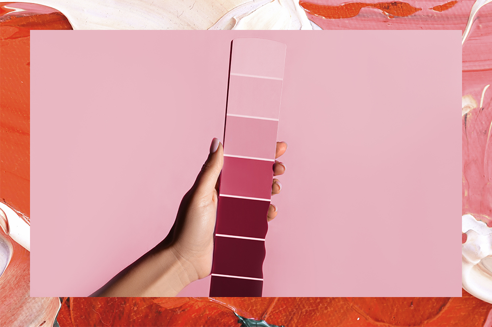 Mão segurando paleta de tons similares ao Viva Magenta; montagem em fundo rosa e vermelho