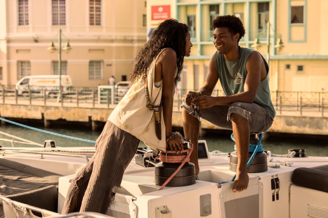 Carlacia Grant como Cleo e Jonathan Daviss como Pope em Outer Banks; eles estão próximos um do outro e se olham sorrindo em um barco