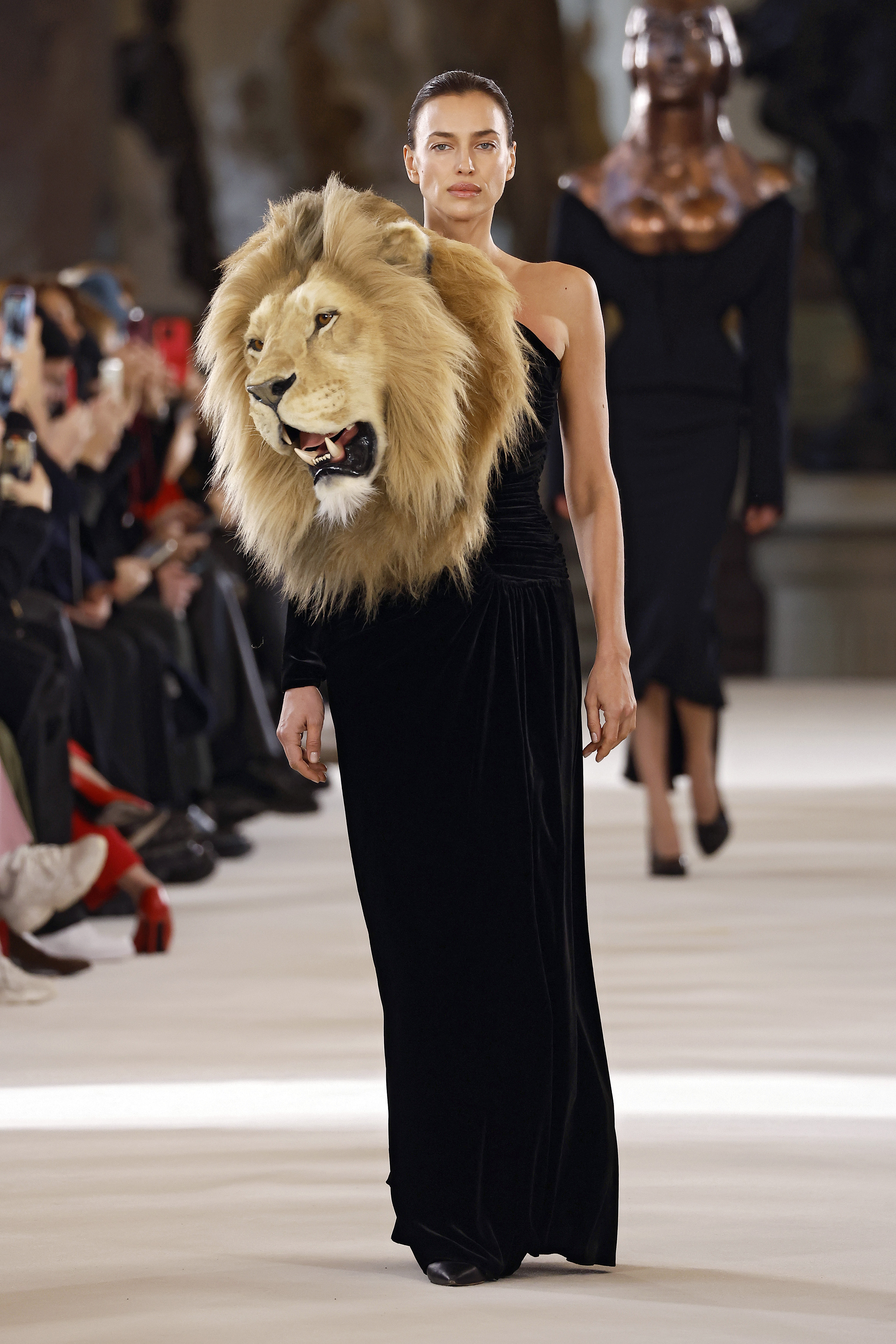 Modelo Irina Shayk desfilando para a Schiaparelli na semana de alta-costura 2023 em Paris com vestido longo preto que possui cabeça de leão