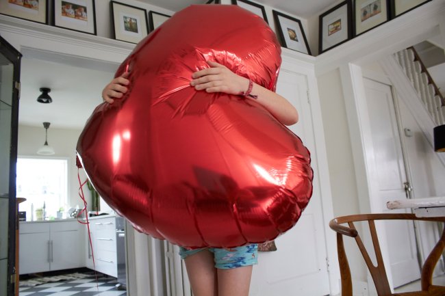 Adolescente segura um balãod e coração gigante. Não dá para ver seu rosto