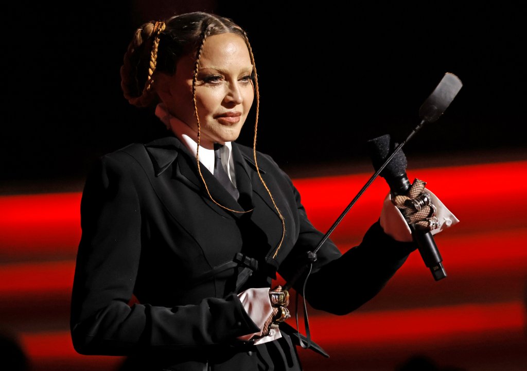 Madonna no palco do Grammy 2023; ela está segurando um microfone com expressão neutra enquanto olha para o público