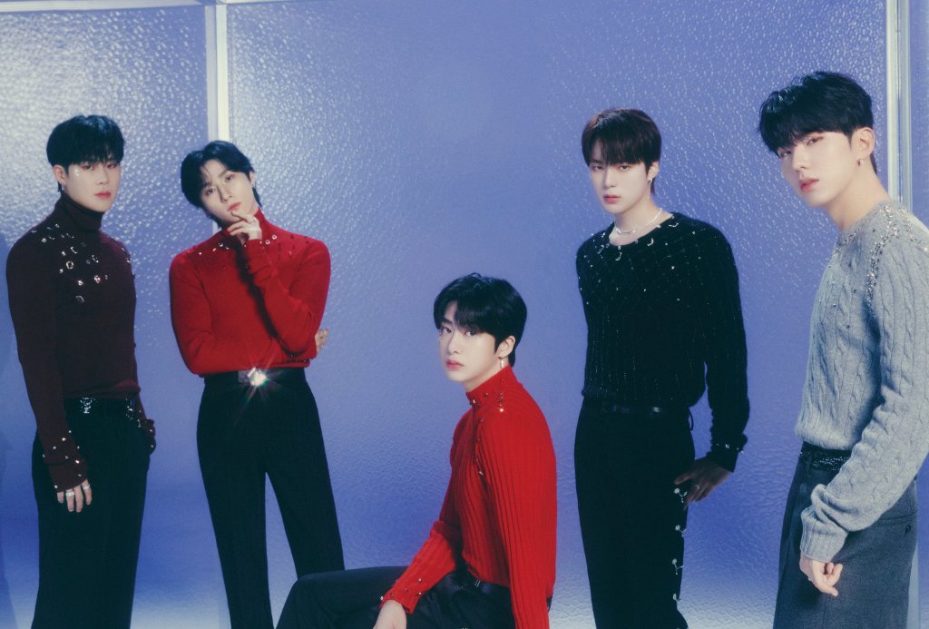 Integrantes do Monsta X posando para foto com expressões neutras em um fundo cinza com iluminação azulada