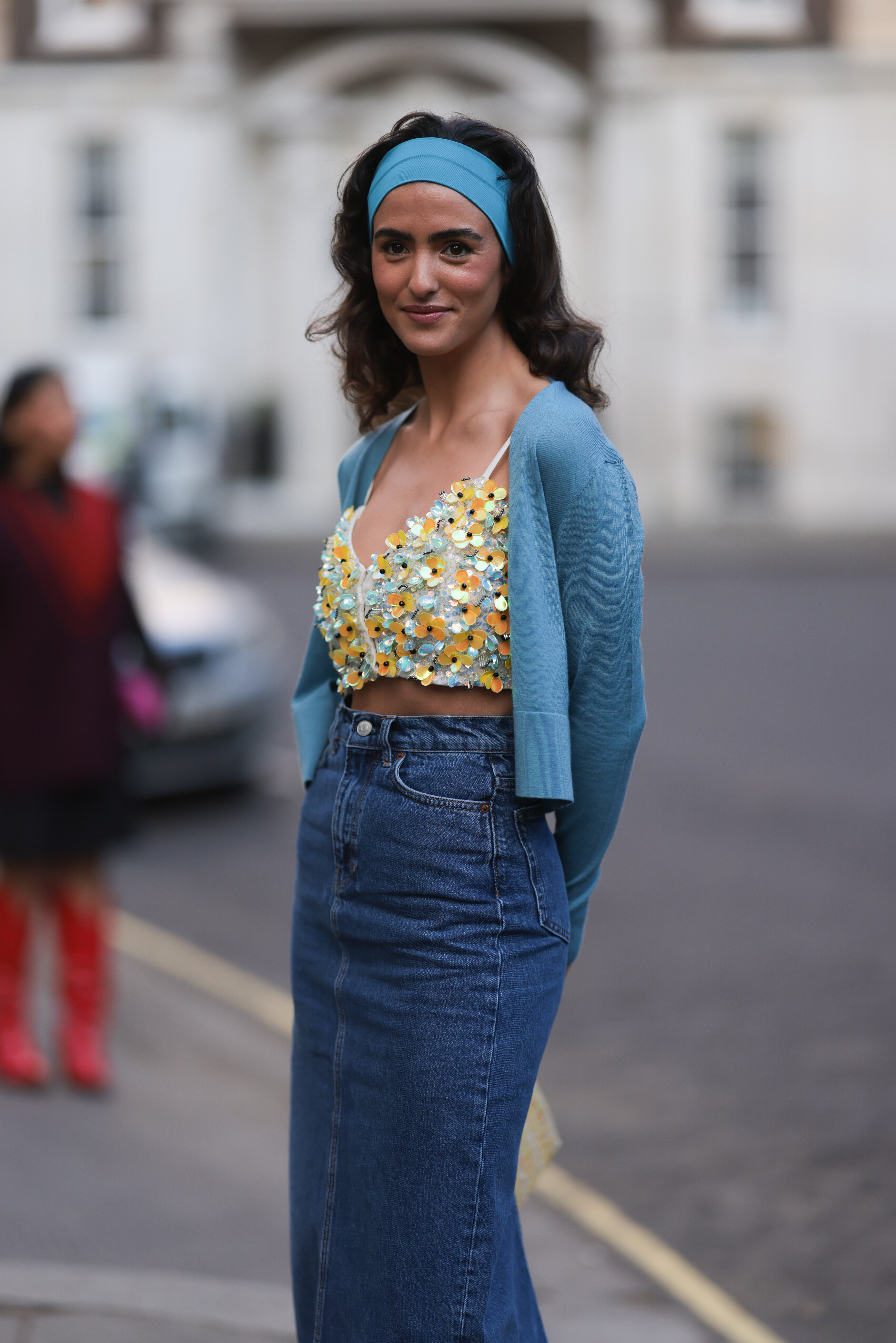 Juny Breeze usando saia jeans, top floral, casaquinho azul e faixa de azul no cabelo no street style da semana de moda de Londres