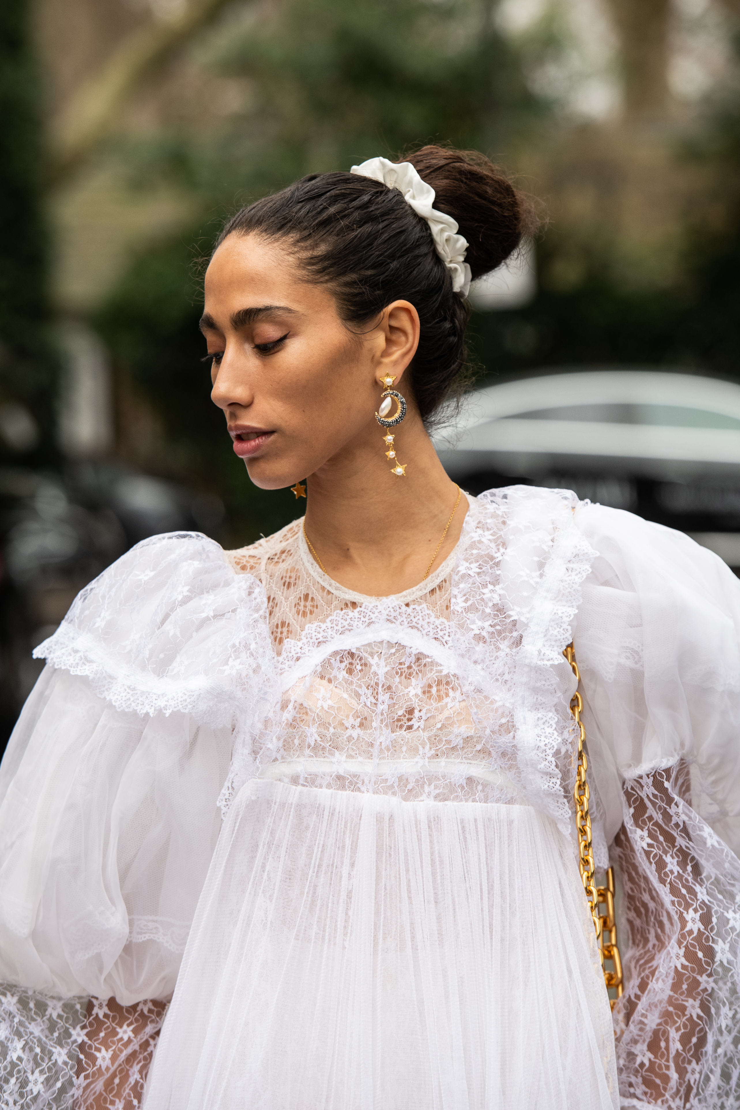 Mulher usando vestido de renda branco e cabelo preso em coque envolto com srunchie no street style da semana de moda de Londres