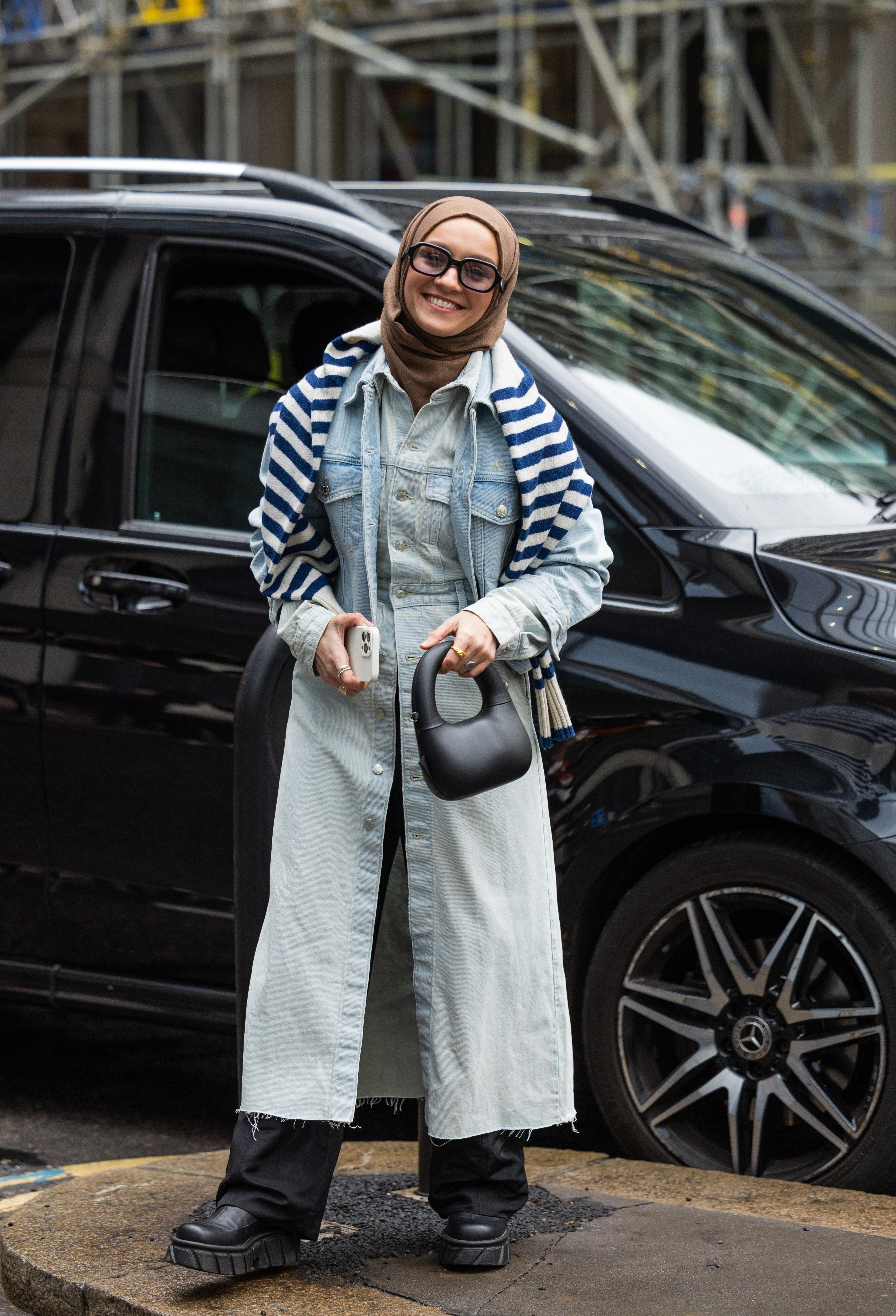 Mulher usando usando vestido jeans por cima de calça preta no street style da semana de moda de Londres