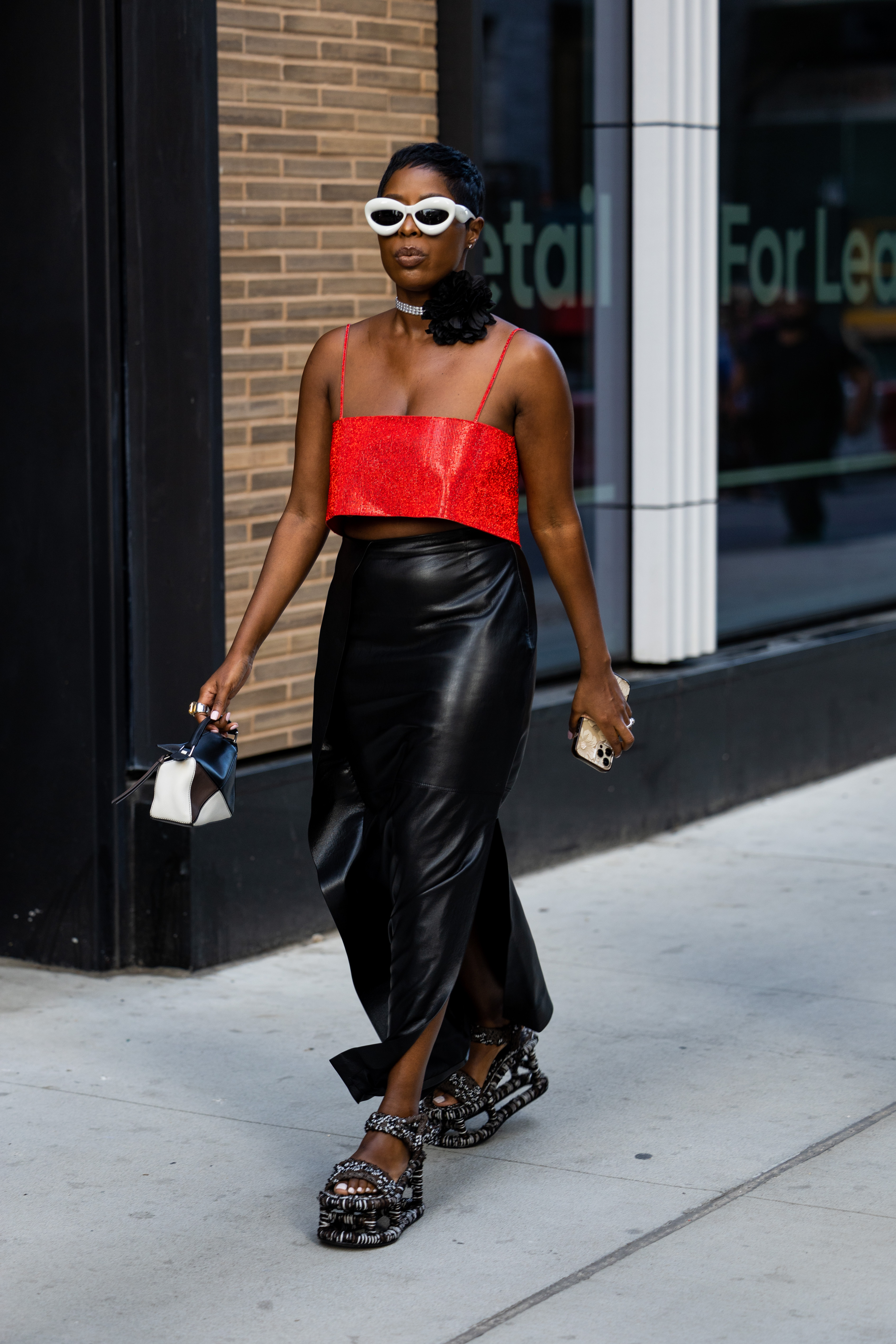 Look com choker de flor no street style da semana de moda de Nova York em setembro de 2022. Mulher também usa top vermelho, saia longa de couro preta e óculos de sol brancos