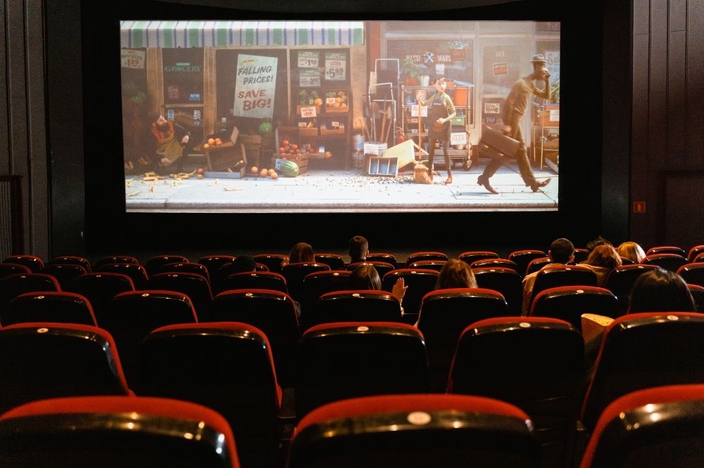 Imagem de um cinema, com cadeiras vermelhas e filme no telão