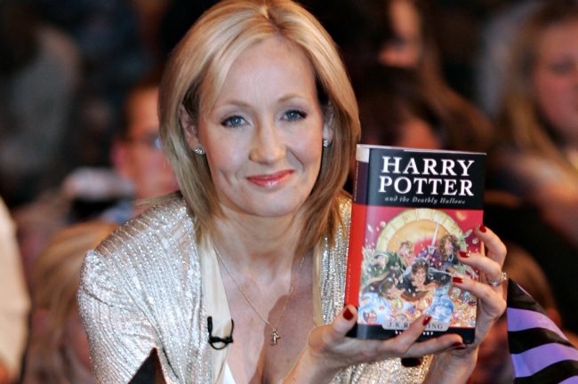 JK Rowling segurando um livro de Harry Potter. Ela é uma mulher branca, loira e alta